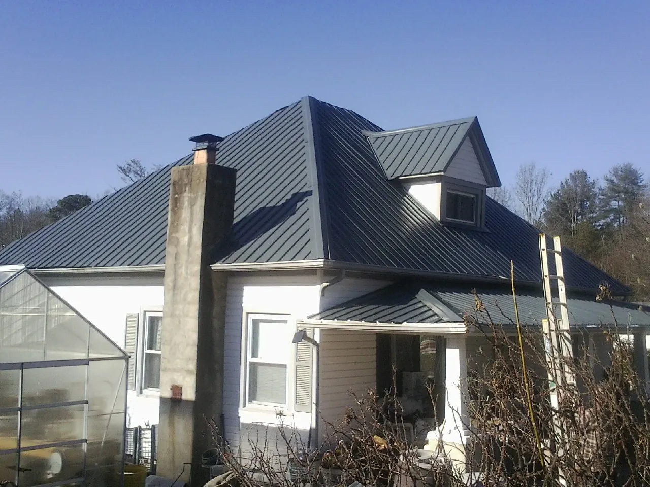 Dark blue standing seam metal roof on a white farmhouse with dormer — Slate & Tile Roof Repair by Roofing Brothers in Grand Lake