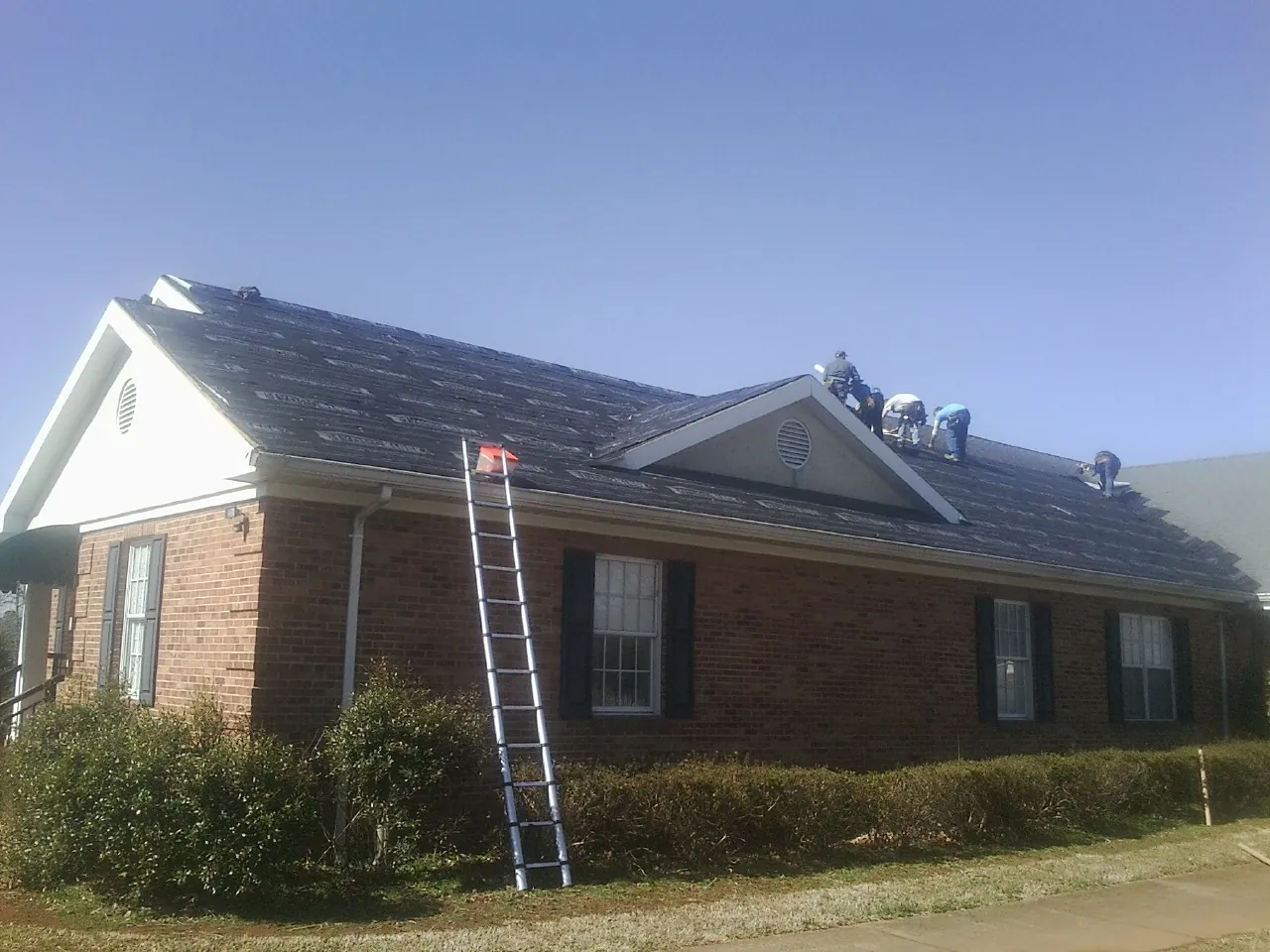 Crew tearing shingles off a brick ranch roof with a ladder set — Metal Roof Repair work by our crew in Grand Lake
