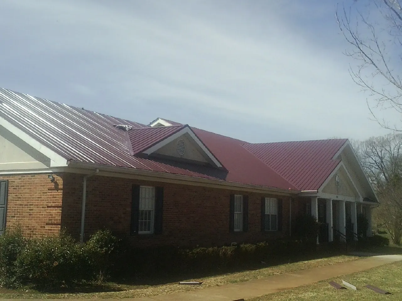Red metal roof with gabled entries on a long brick building, from a Hail Damage Roof Repair job in Grand Lake