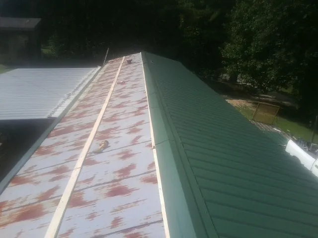 Old rusted panels beside newly installed green metal roofing — Wind Damage Roof Repair by Roofing Brothers in Grand Lake