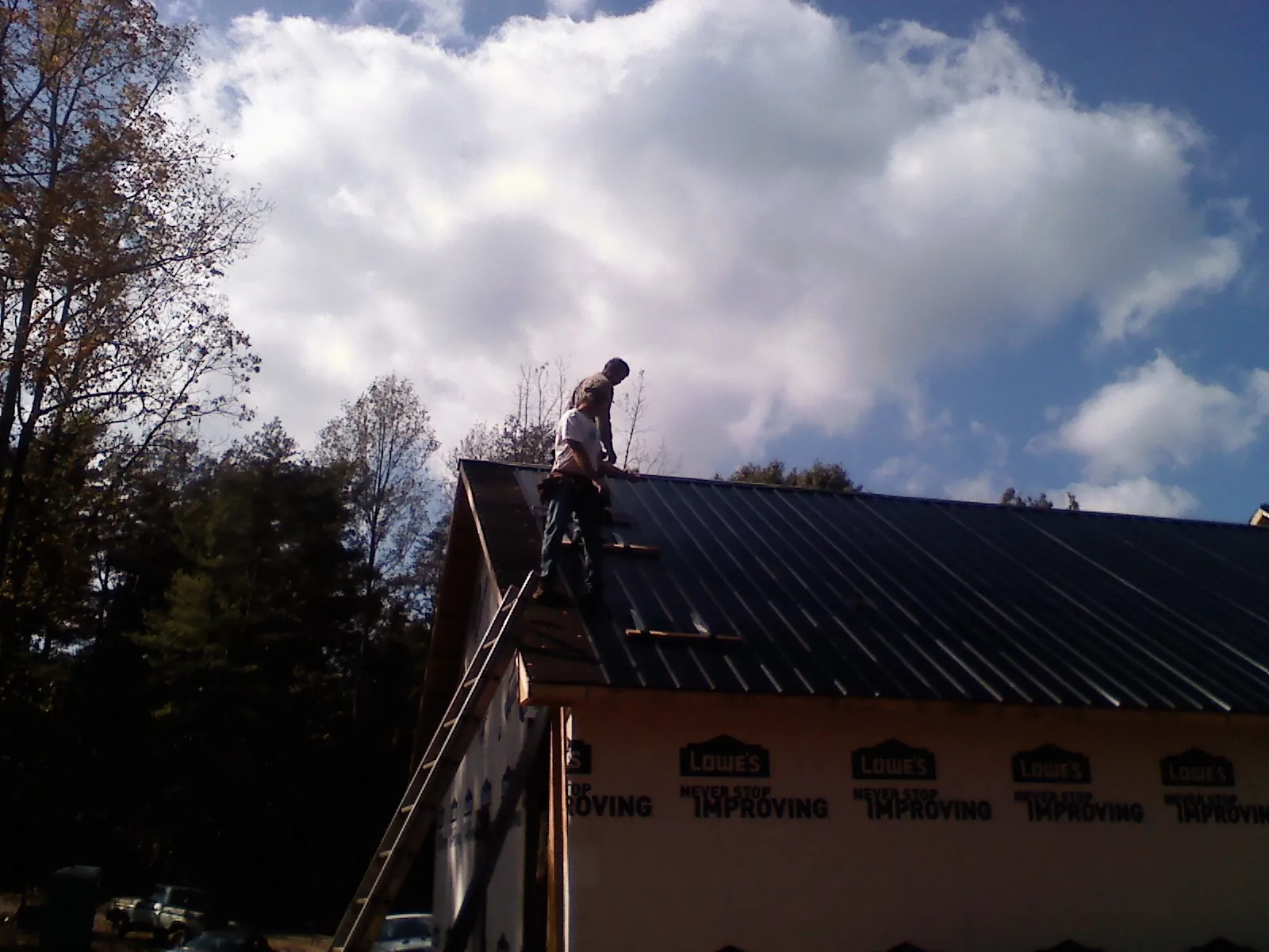 Roofer fastening dark metal panels high against a cloudy sky, from a Roof Inspection job in Grand Lake