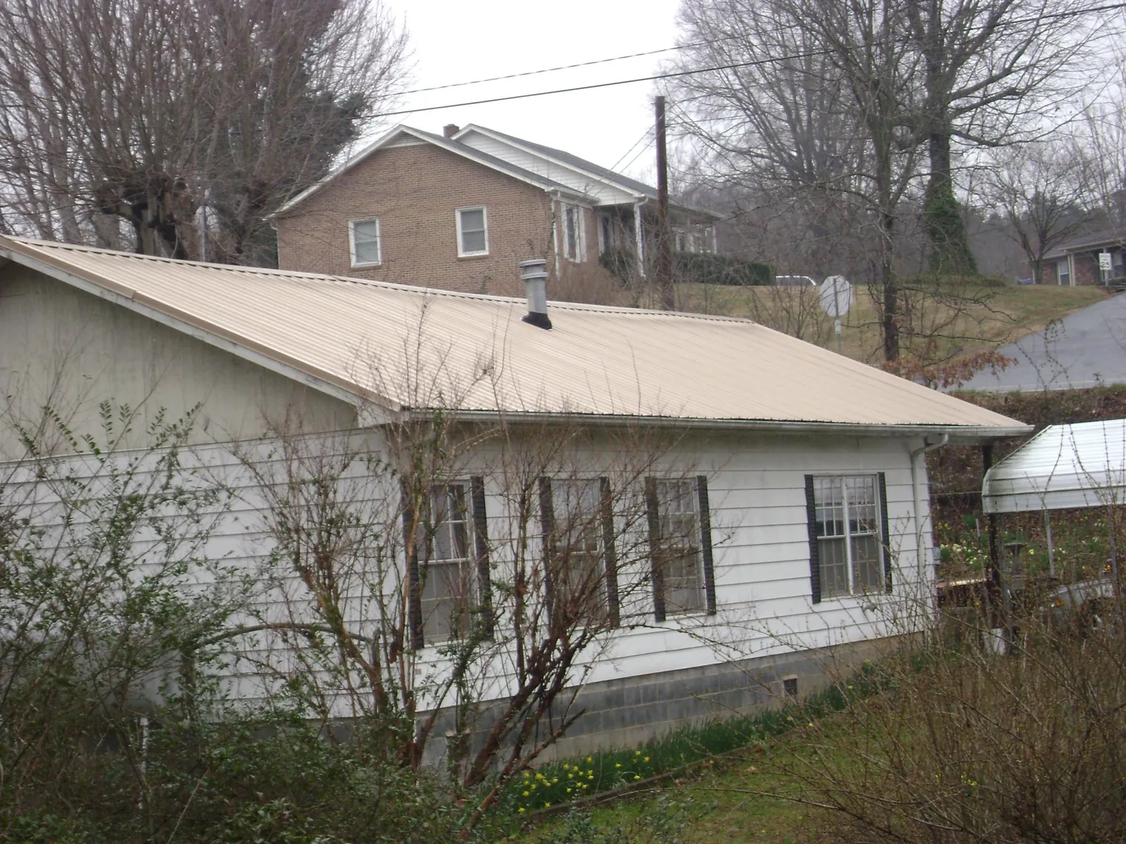Tan metal roof on a white sided house set into a hillside — Commercial Roofing by Roofing Brothers in Grand Lake
